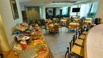 Un espace repas avec plusieurs tables et chaises, un buffet proposant divers plats et un téléviseur fixé au mur.