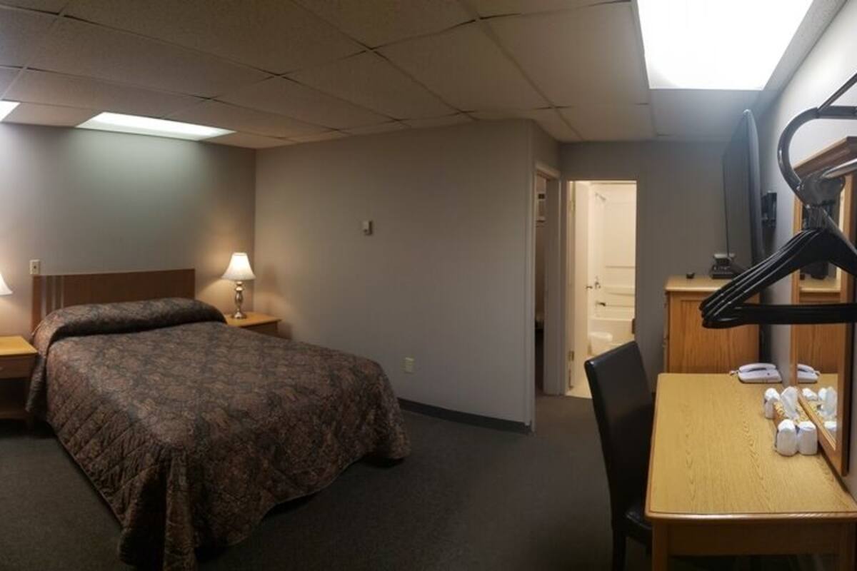 A hotel room with a bed, two bedside tables with lamps, a desk with a chair, a mirror, and a coat rack.