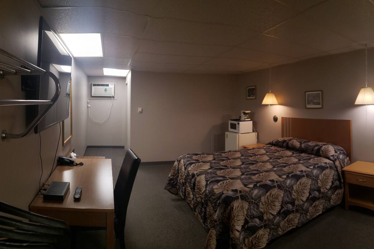 A hotel room with a bed, bedside table, desk, chair, and a small round table.