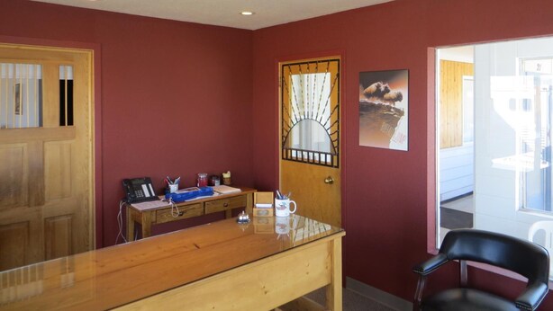 A room with a wooden desk, a black leather chair, a wooden door with a decorative glass panel, and a poster on the wall. - Sunset Motel (Fort Macleod)