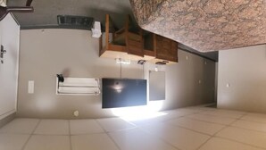 A room with a tiled floor, a flat-screen TV mounted on the wall, and a wooden cabinet under the ceiling. - Sunset Motel (Fort Macleod)