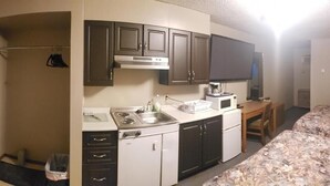 A compact hotel room with a kitchenette, a bed, a television, and a shower area. - Sunset Motel (Fort Macleod)