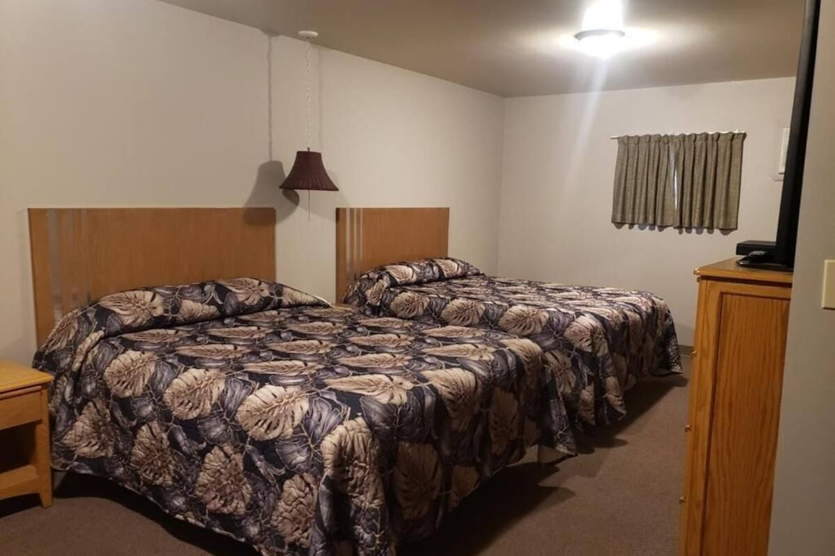 A bedroom with two beds, a wooden headboard, a bedside table, a lamp, and a curtain.
