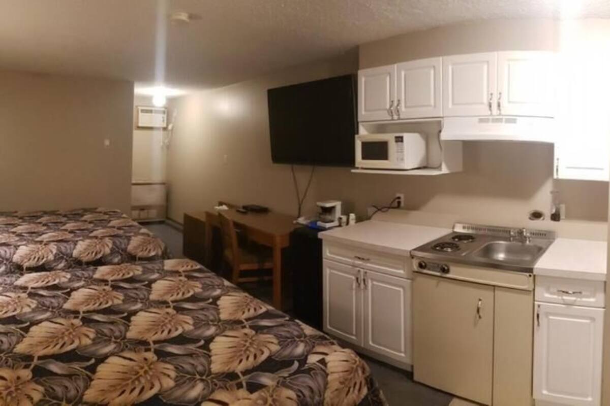 A small room with a bed, a desk, a microwave, a stove, and a sink.