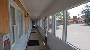 A corridor with wooden paneling on one side and large windows on the other, leading to a parking area. - Sunset Motel (Fort Macleod)
