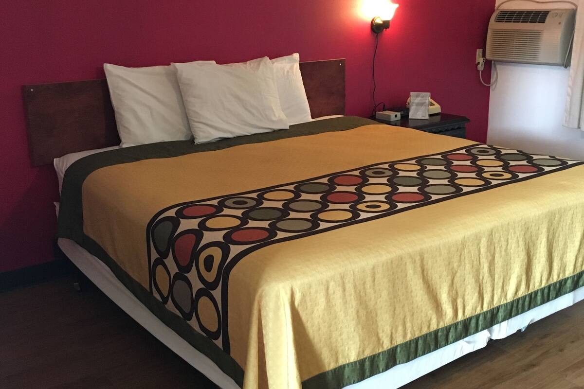 A bed with a patterned bedspread, a bedside table with a lamp, and an air conditioning unit on the wall.
