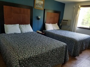 Two single beds with patterned bedspreads, a wooden headboard, a wall-mounted telephone, and a window with curtains.