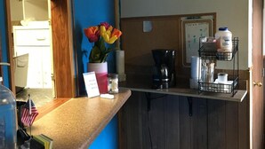 A counter with a coffee maker, a water dispenser, and a sign that says "Please fill the bucket for service." - Tarragon Motel (Marinette)