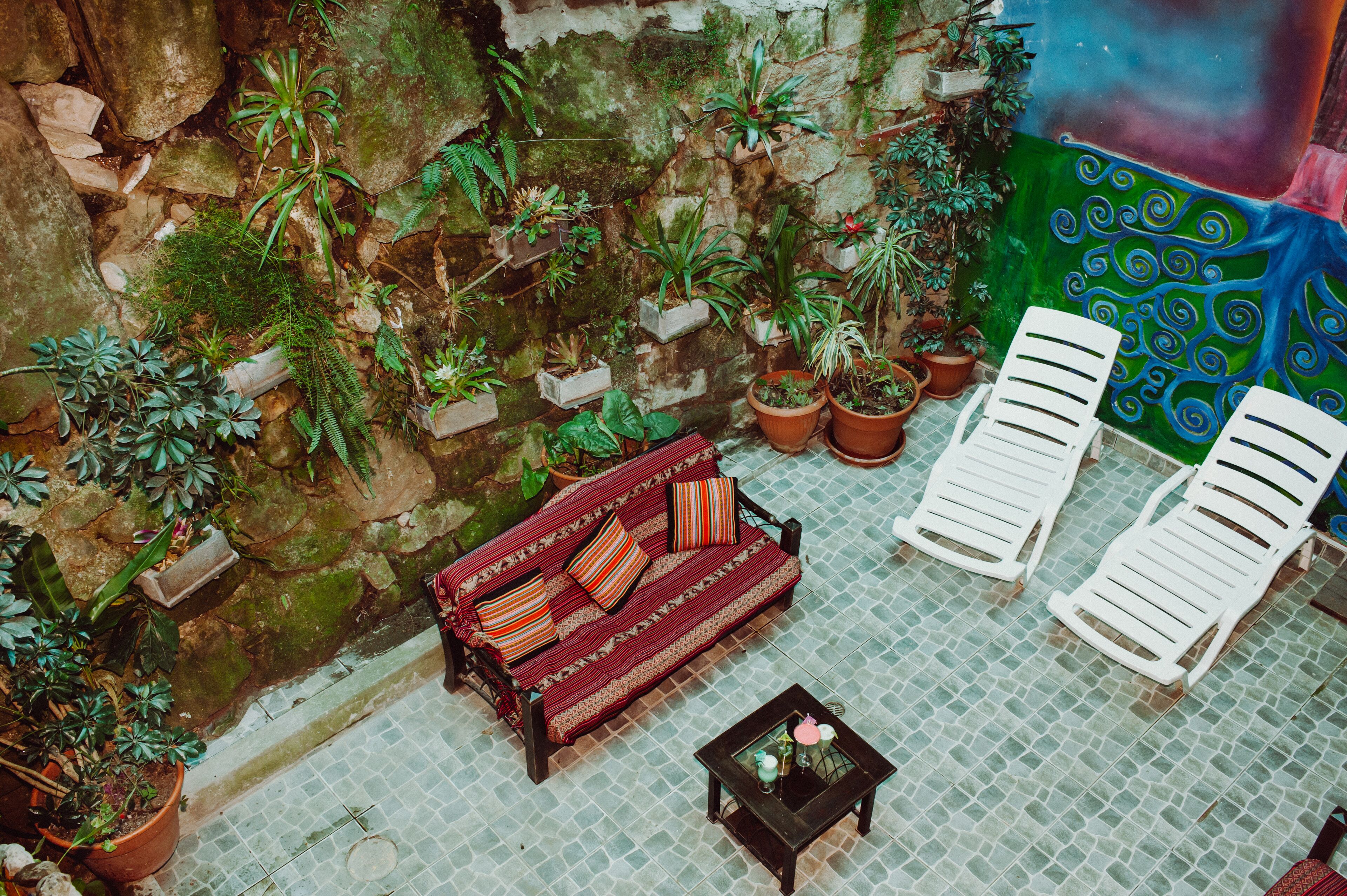 A cozy outdoor seating area with a sofa and two lounge chairs, surrounded by potted plants and a decorative wall.