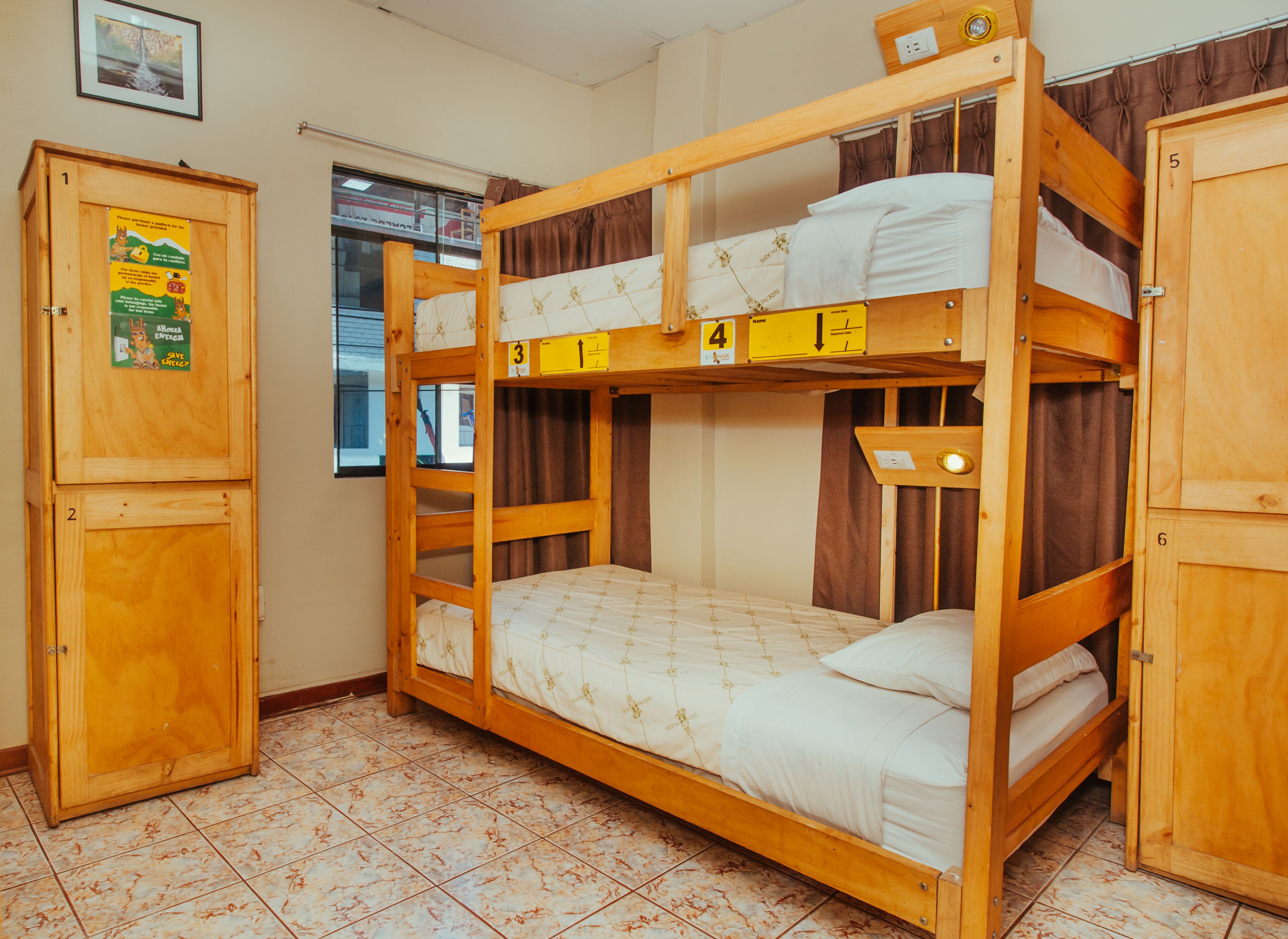 Habitación con literas de madera, un armario y una ventana con cortinas.
