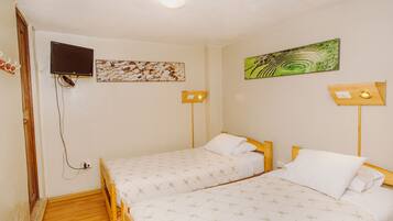 Una habitación con dos camas, un televisor montado en la pared y dos lámparas de pared.