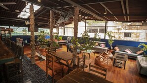 A spacious indoor area with wooden furniture, large windows, and potted plants. - Nativus Hostel Machu Picchu (Machu Picchu)