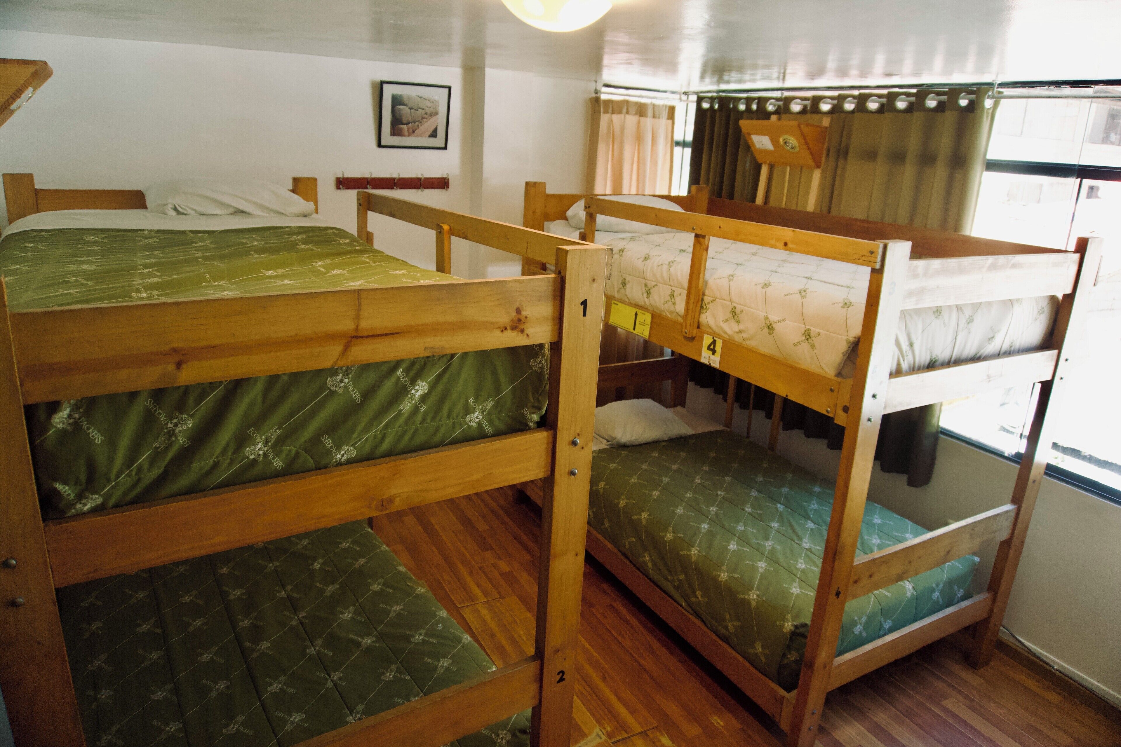 A room with bunk beds, wooden flooring, a framed picture on the wall, and a window with curtains.