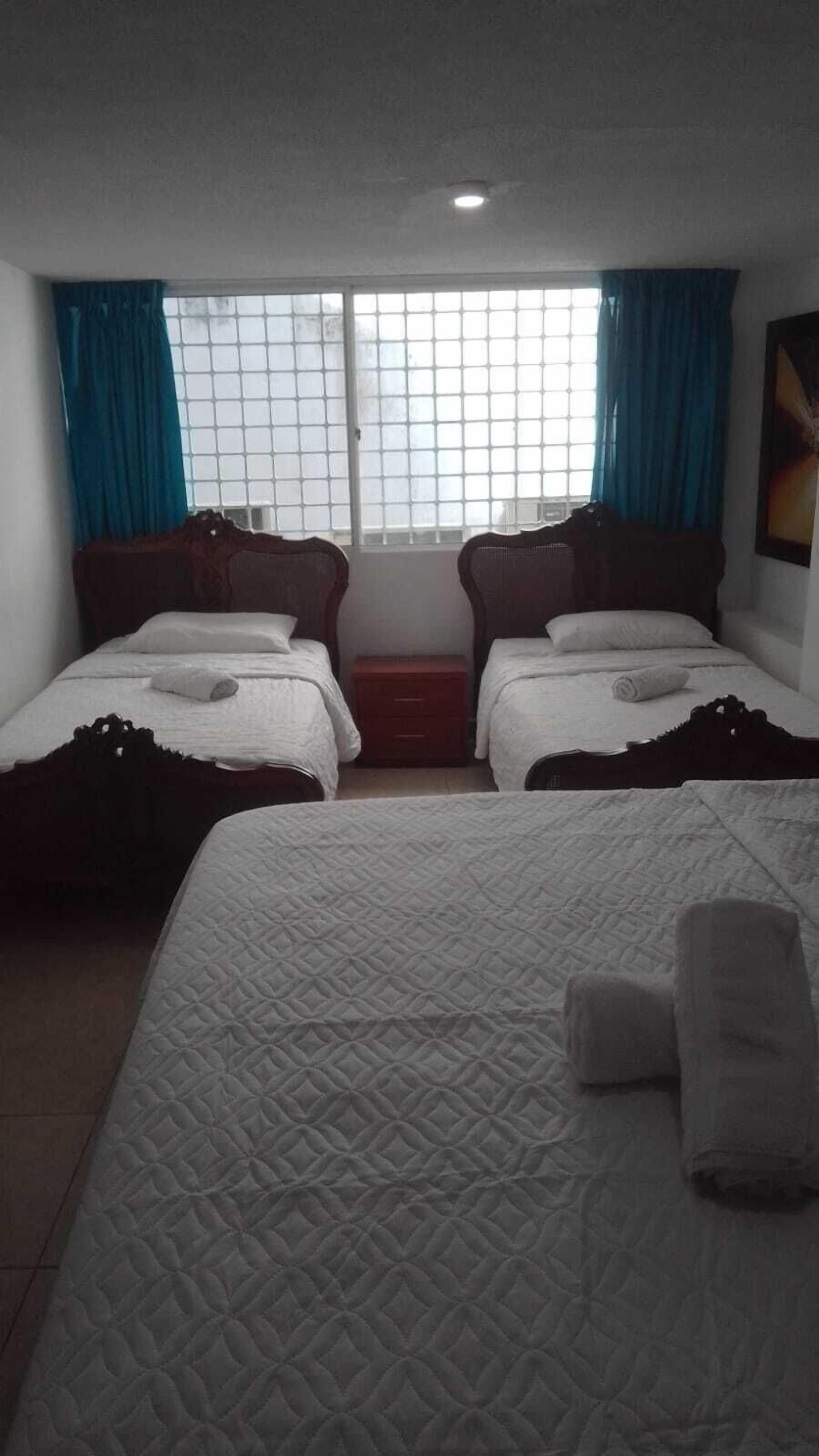 Habitació d'hotel amb dos llits individuals, un llit més gran, una finestra amb cortines i un petit armari.