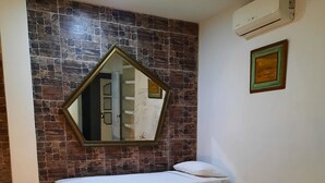 Une chambre d’hôtel comprenant un lit, un petit coin salon, un mur en pierre, un miroir et un appareil de climatisation.