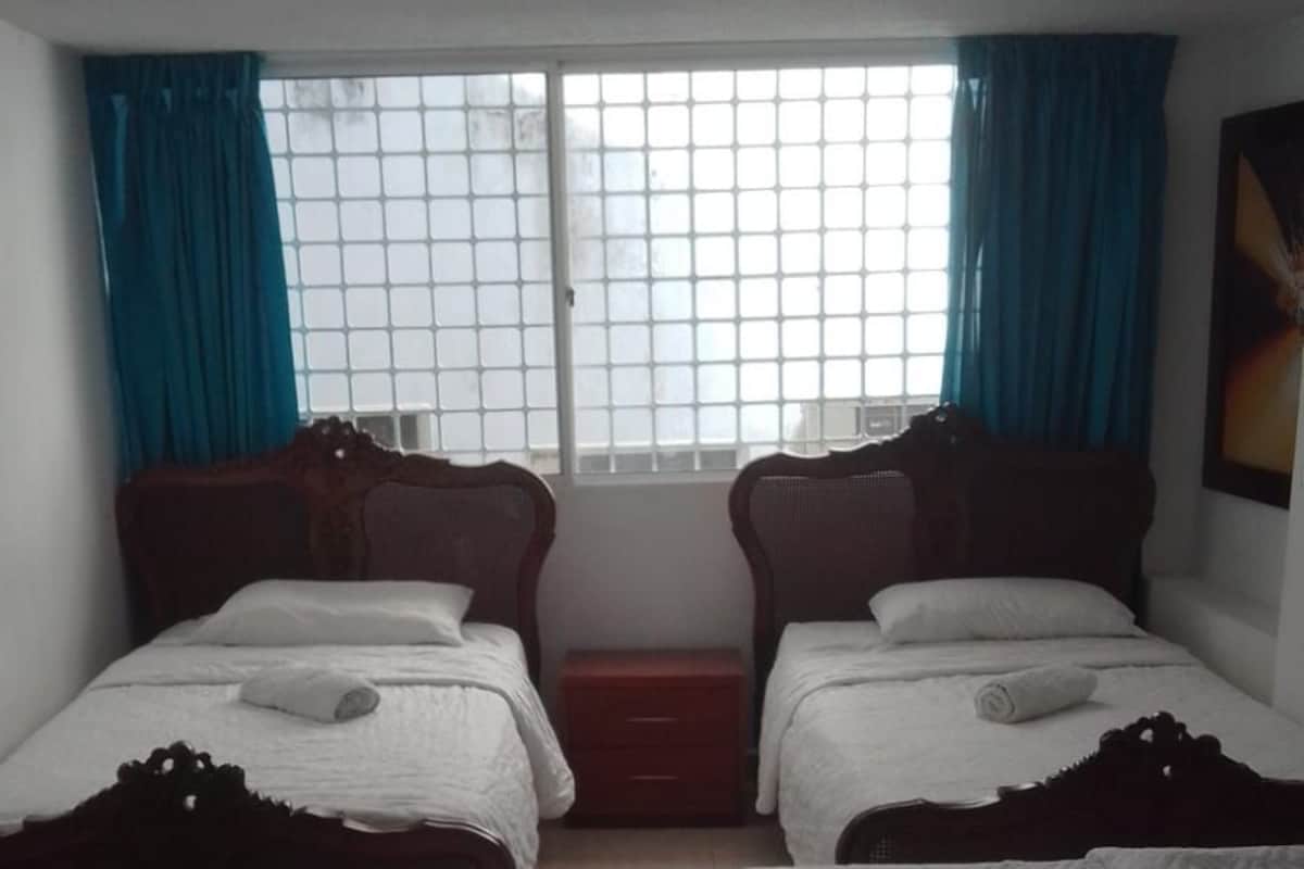 Hotellihuone, jossa on kaksi erillistä sänkyä, yksi suurempi sänky, ikkuna verhoilla ja pieni kaappi.