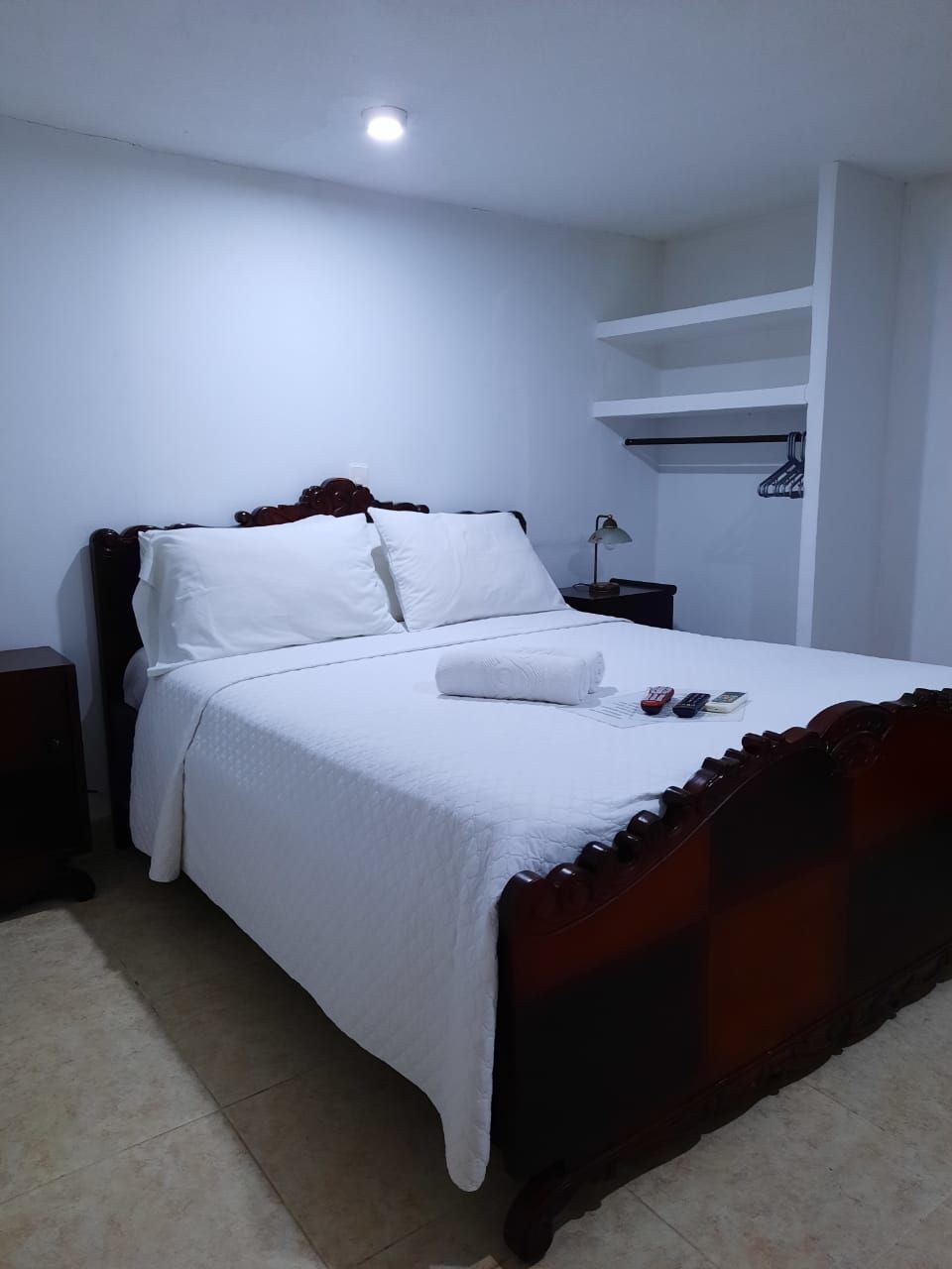 Habitación estándar de hotel con una cama individual, una mesita de noche, una lámpara y estantería empotrada.