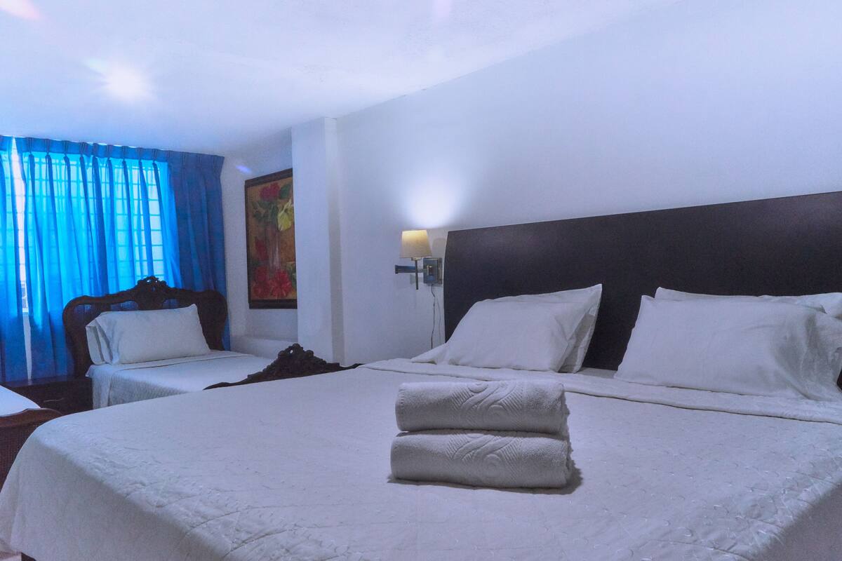 Habitación de hotel con dos camas, una mesita de noche, una lámpara y un cuadro en la pared.