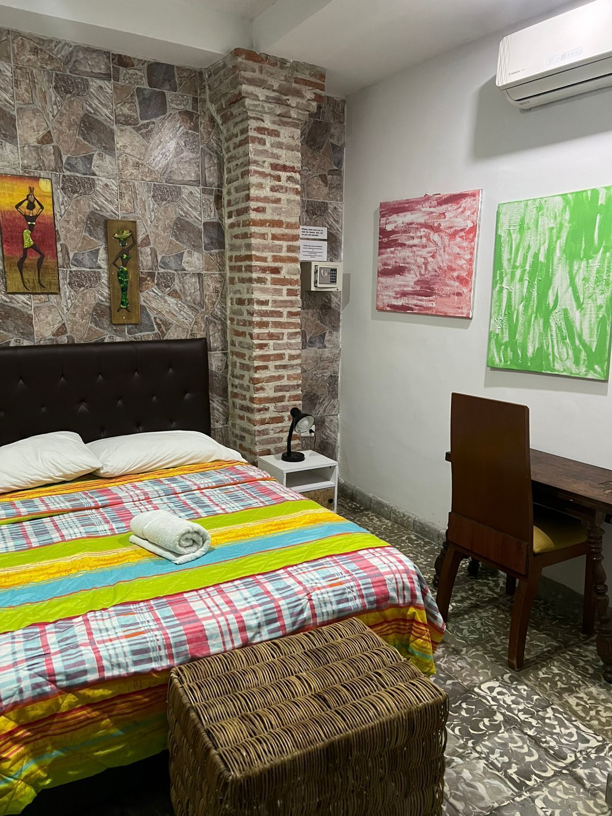 A bedroom with a bed, a desk, and a chair. There is a stone wall and a brick column.
