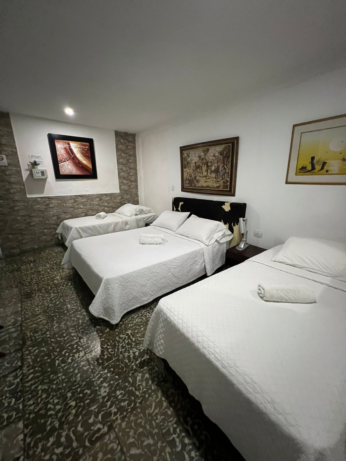 Habitació d'hotel amb dos llits, una paret de pedra i obres d'art a les parets.