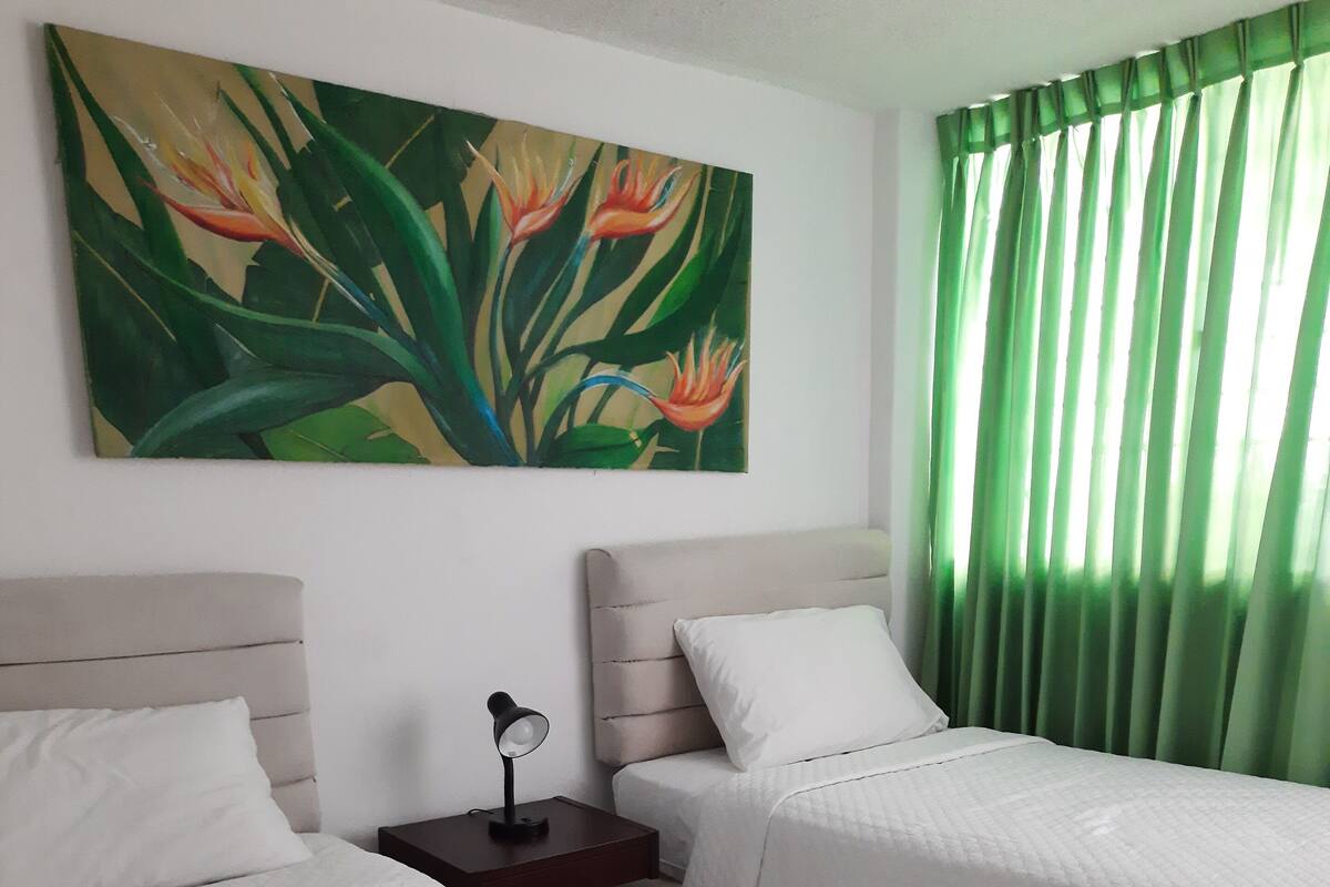 Habitación de hotel con dos camas, una mesita de noche, una lámpara y un cuadro en la pared.