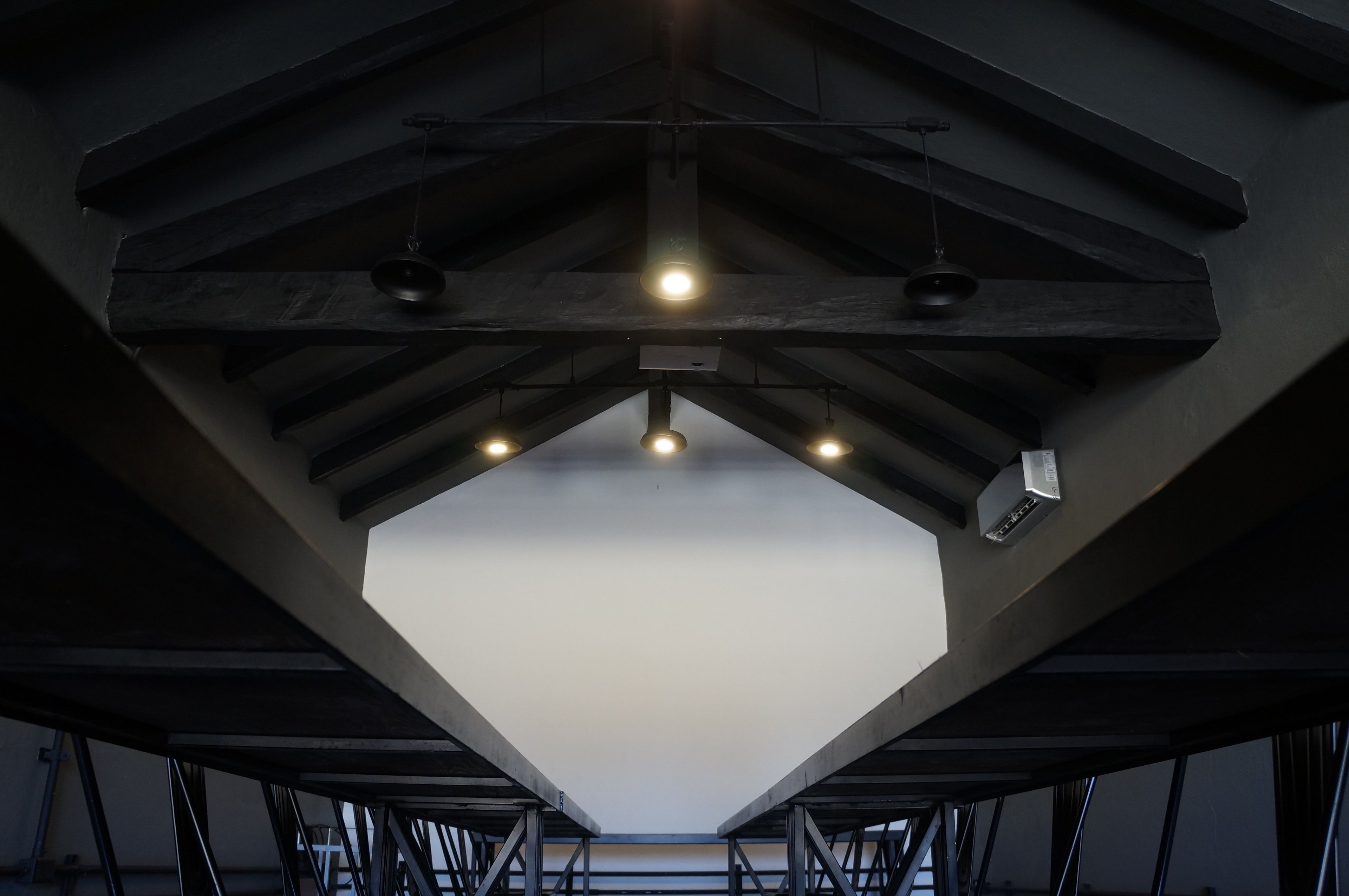 A geometric ceiling structure with exposed beams and hanging lights.