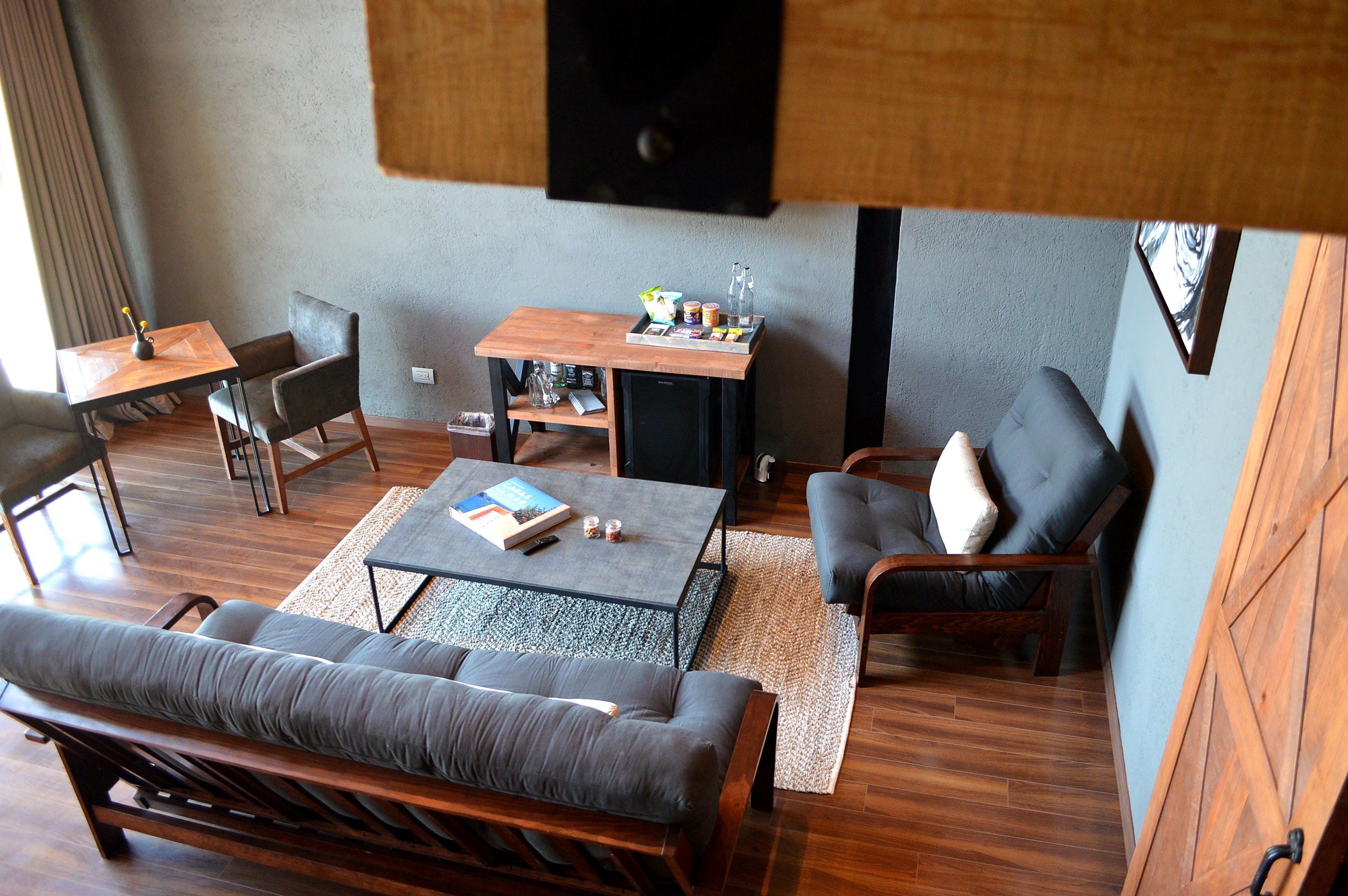 A modern living room with a sofa, coffee table, and chairs. There is a small table with a tray of items and a speaker mounted on the wall.