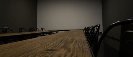 A conference room with a long wooden table, several chairs, and a large blank screen at the front.