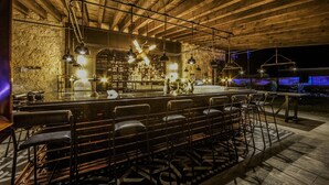 A bar area with high ceilings and exposed beams, featuring a bar counter, multiple bar stools, and pendant lighting. - Hacienda Los Picachos (San Miguel de Allende)