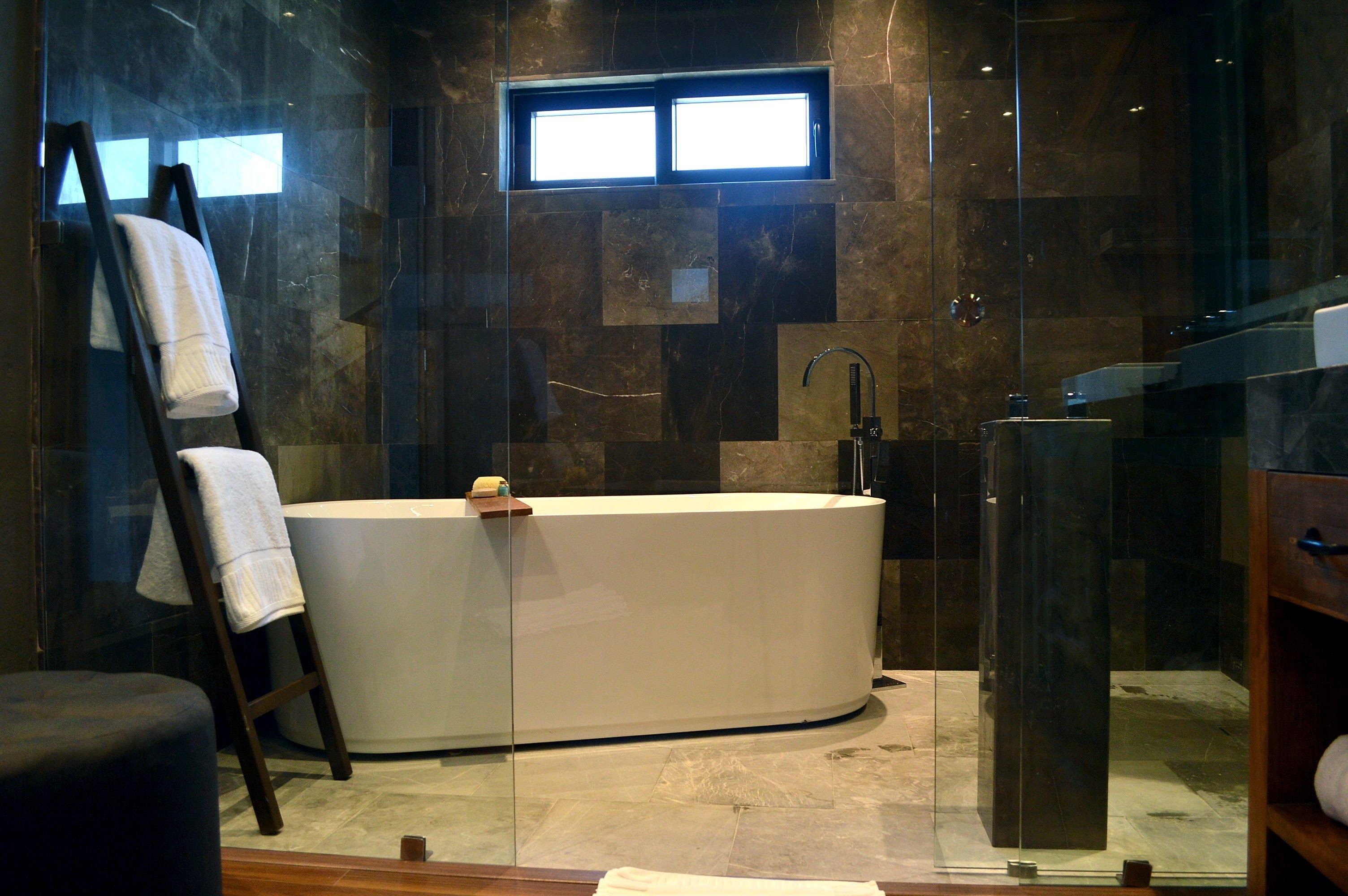 A modern bathroom with a freestanding bathtub, a glass shower enclosure, and a small window providing natural light.