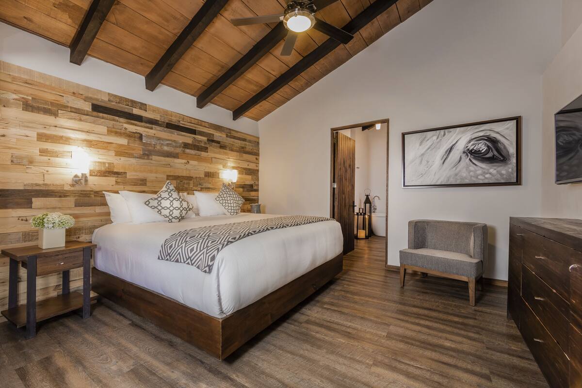 A bedroom with a wooden headboard, a large bed, bedside tables, a chair, and artwork on the walls.