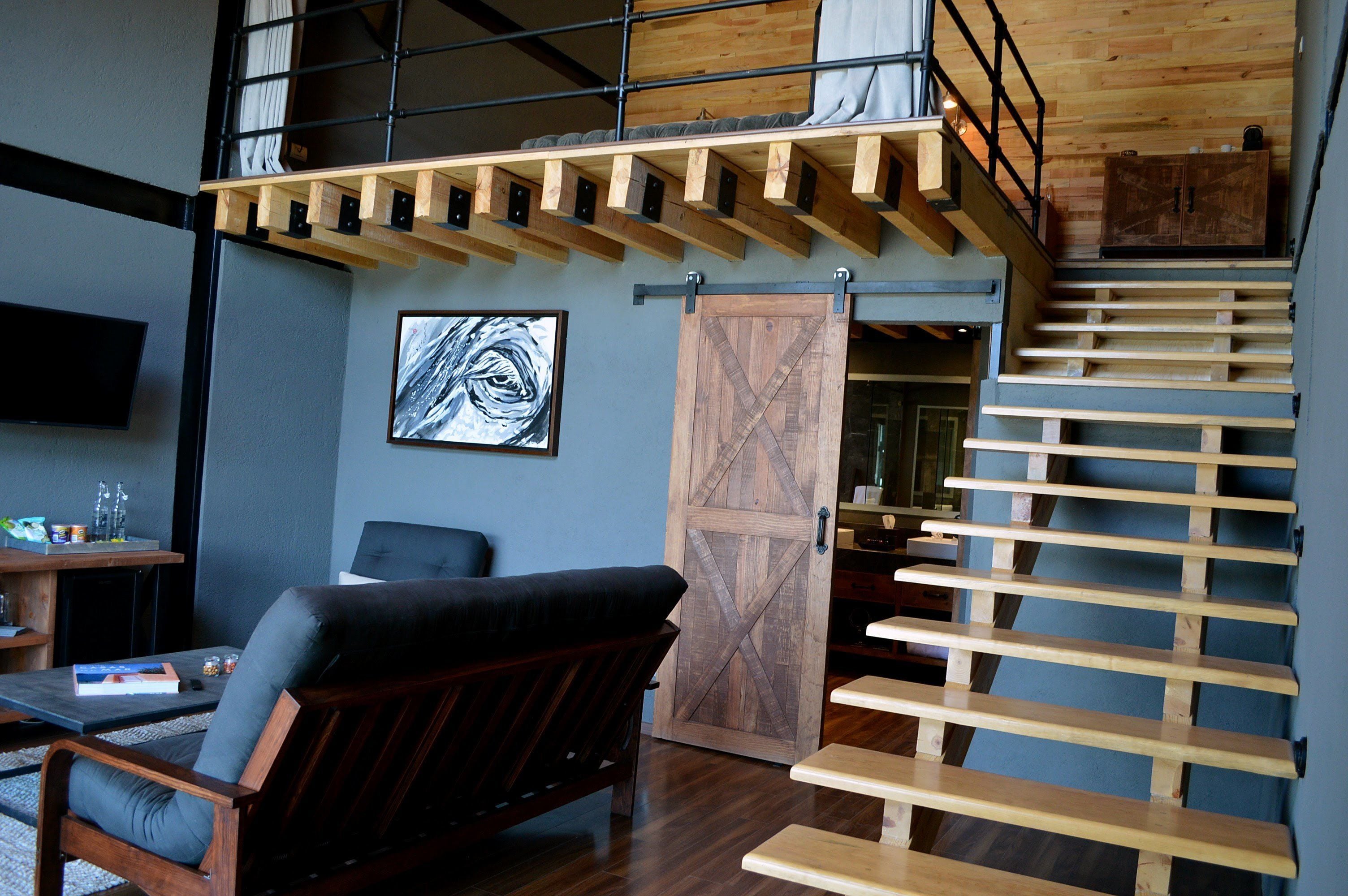 Un espacio tipo loft con escalera de madera, un amplio puertas correderas tipo granero y un sofá de cuero negro.
