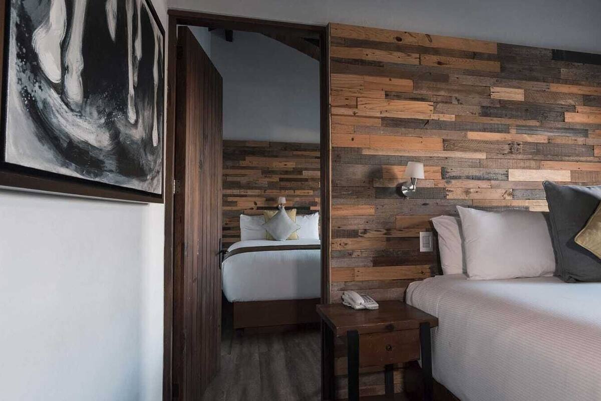 A hotel room with a wooden headboard, a bed with white bedding, a bedside table with a lamp, and a painting on the wall.