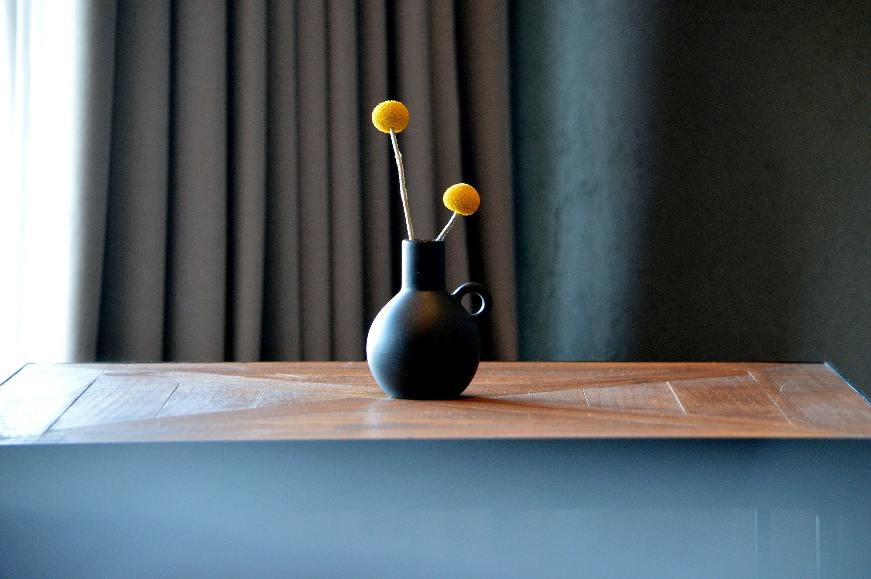 A black vase with two yellow spherical objects on a wooden surface.