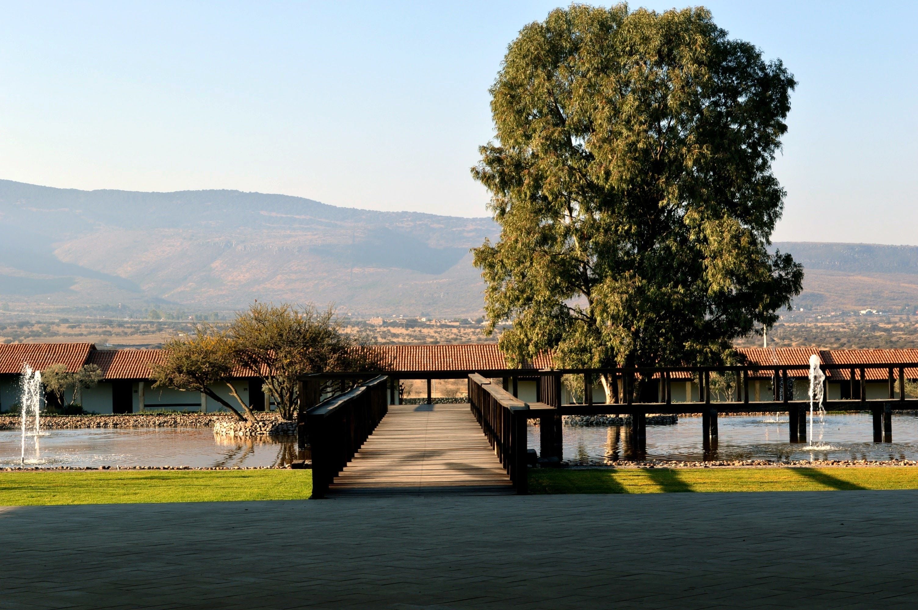 A wooden bridge leading to a building with a tiled roof, overlooking a body of water and distant hills.