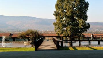 A wooden bridge leading to a building with a tiled roof, overlooking a body of water and distant hills.
