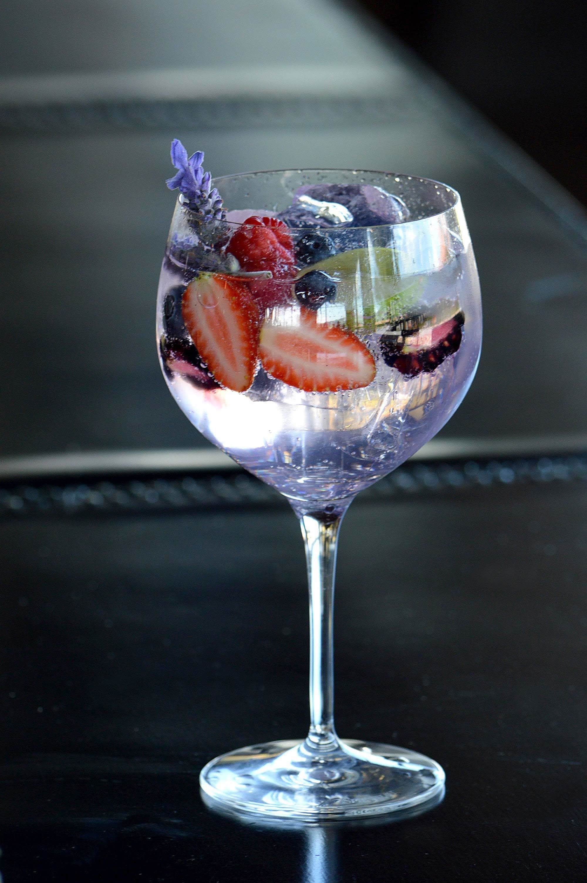 A clear glass with a strawberry and a purple flower on a reflective surface.