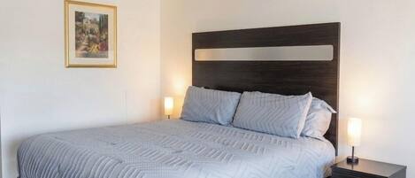 A neatly made bed with a dark headboard, two bedside tables with lamps, and a framed picture on the wall.