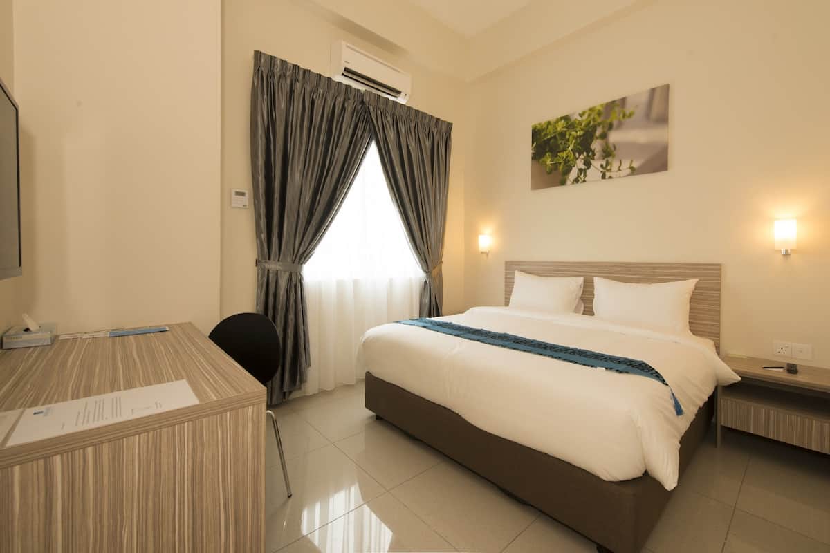Habitación de hotel con cama, mesitas de noche, escritorio, silla, aire acondicionado y ventana con cortinas.