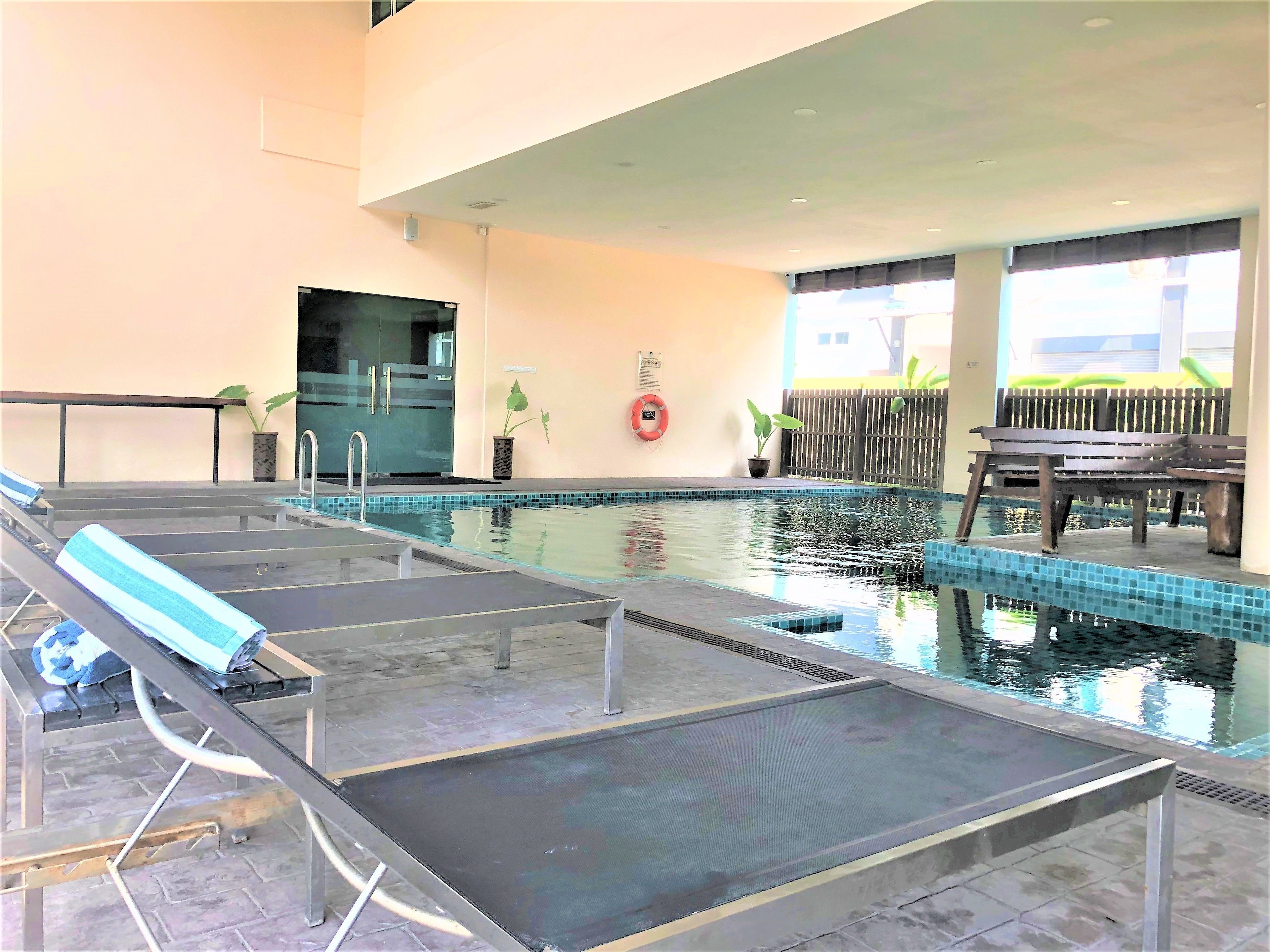 An indoor swimming pool with lounge chairs, a wooden bench, and potted plants.