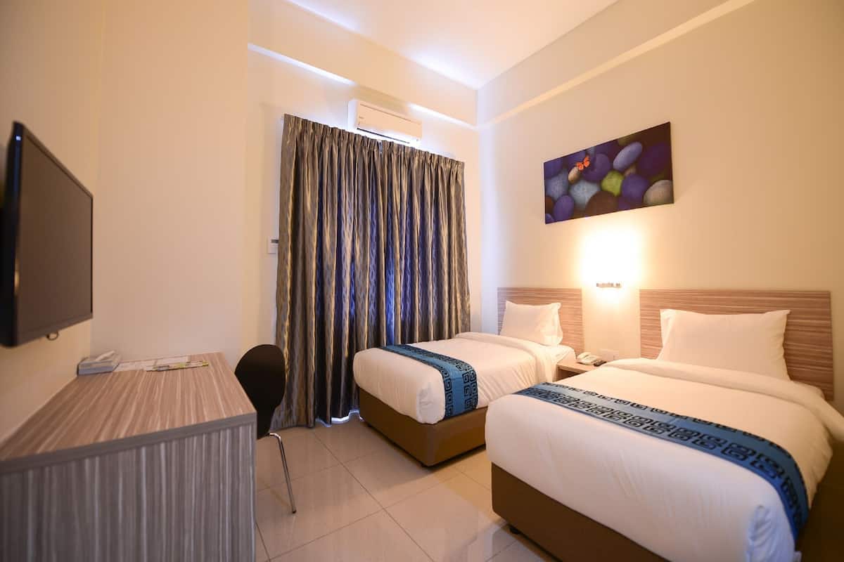 Habitación de hotel con dos camas, un escritorio, una silla, un equipo de aire acondicionado y un cuadro en la pared.