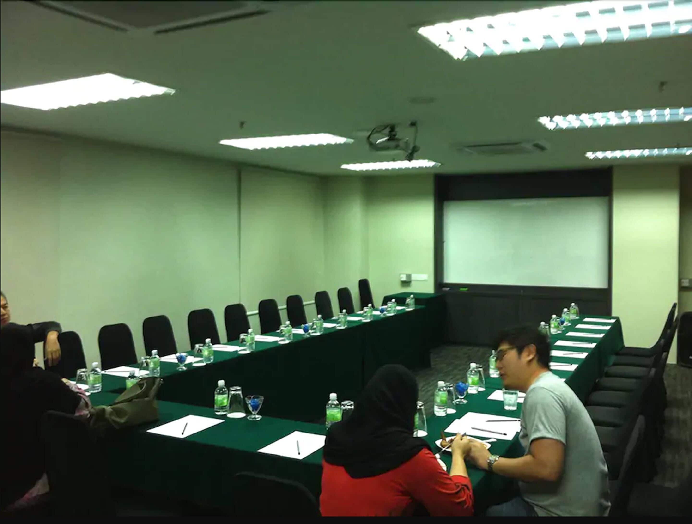 A conference room with a long table, chairs, and a projector screen.