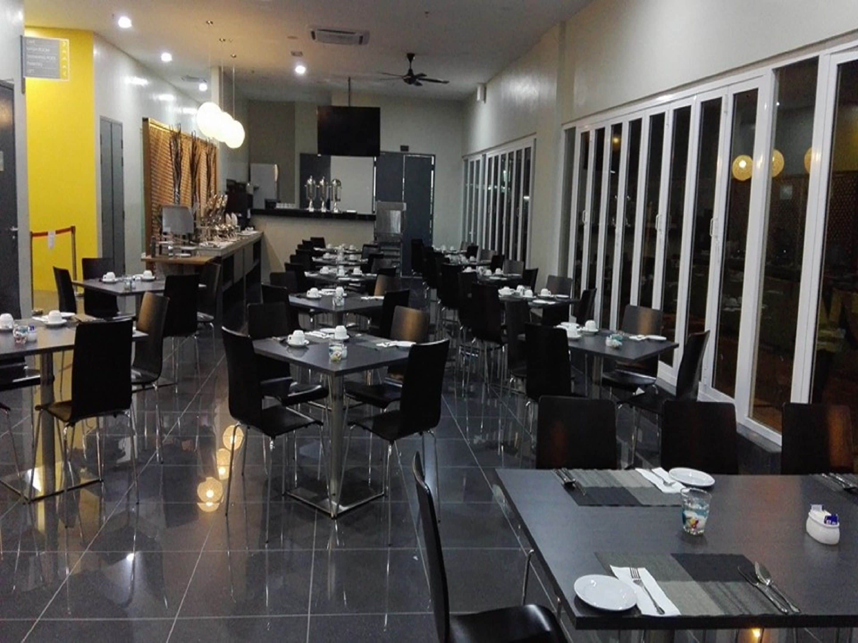 A modern restaurant with black chairs and tables, a bar area, and large windows.