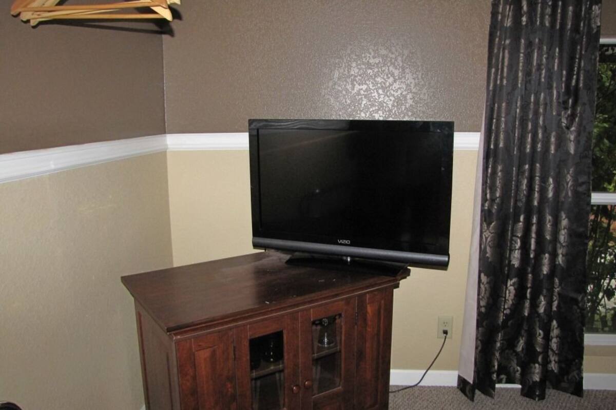 A flat-screen TV on a wooden cabinet in a room with beige walls and a window with curtains.