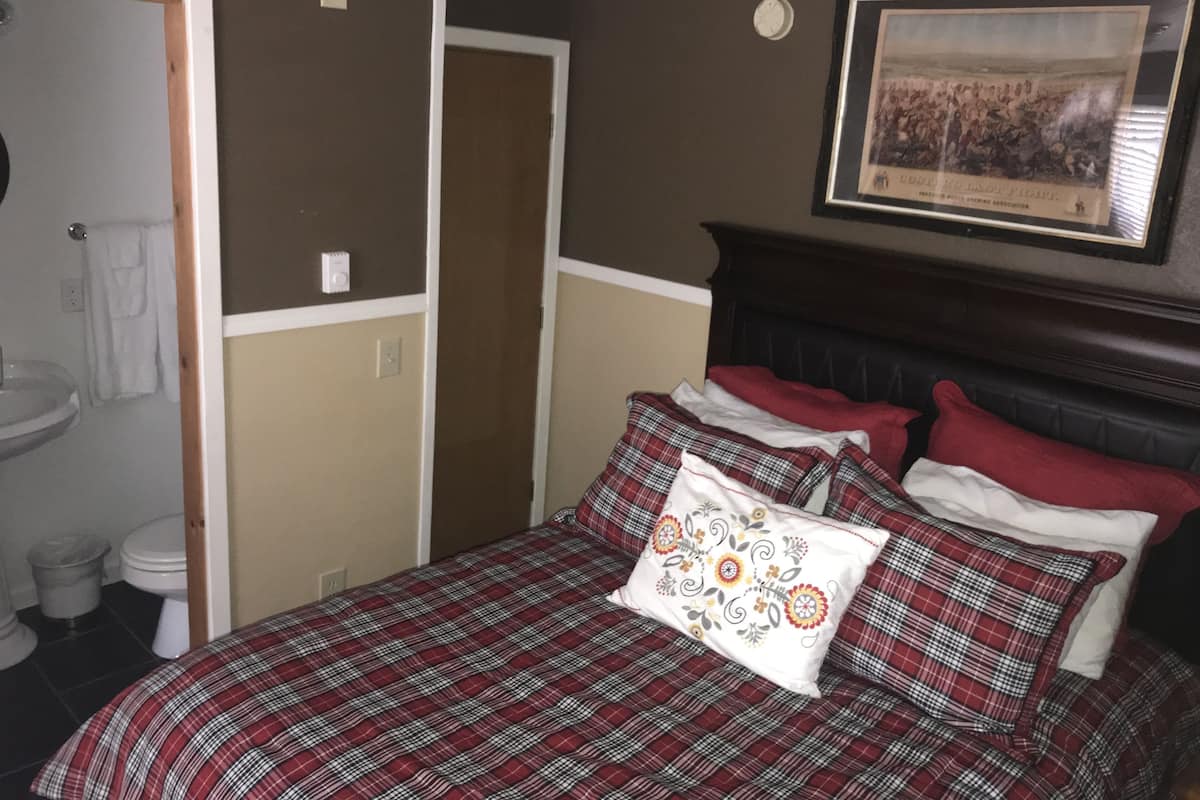 A bedroom with a bed, a framed picture on the wall, and a bathroom visible through an open door.