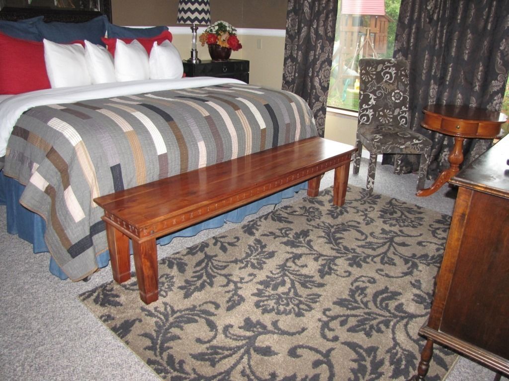 Une chambre à coucher avec un lit, un banc en bois, un tapis à motifs, une chaise et une table.