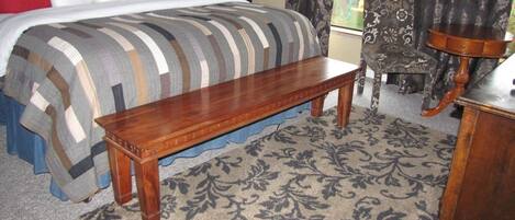 Une chambre à coucher avec un lit, un banc en bois, un tapis à motifs, une chaise et une table.