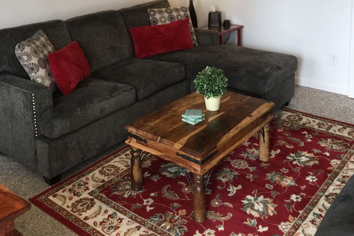 A living room with a grey sofa, red and patterned cushions, a wooden coffee table with a plant, a lamp, and a wall-mounted horse decoration.