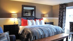 Une chambre à coucher avec un grand lit, deux tables de chevet, un banc, une chaise, un miroir et des rideaux à motifs.