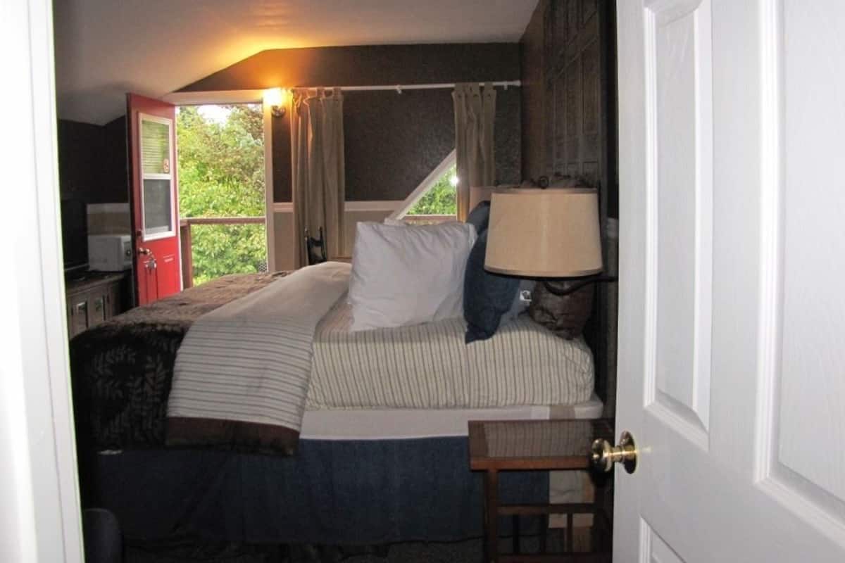 A bedroom with a bed, a nightstand, a lamp, and a window with curtains.